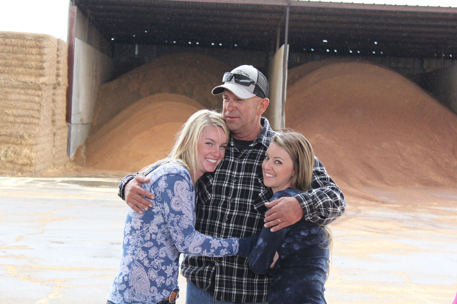 Lexie and Tara give their dad a hug in front of the feed ingredients for the herd.